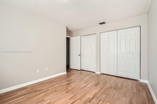 7451 SW 157th Ct, Miami, FL 33193 - unfurnished bedroom with light wood finished floors, a textured ceiling, multiple closets, baseboards, and visible vents