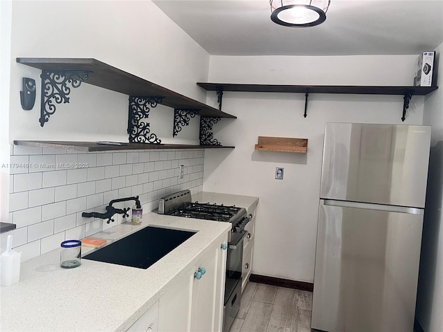 kitchen with decorative backsplash, appliances with stainless steel finishes, open shelves, a sink, and light wood-style flooring
