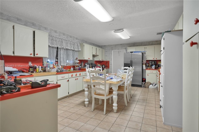 kitchen featuring a textured ceiling, light countertops, a sink, stainless steel fridge, and light tile patterned flooring