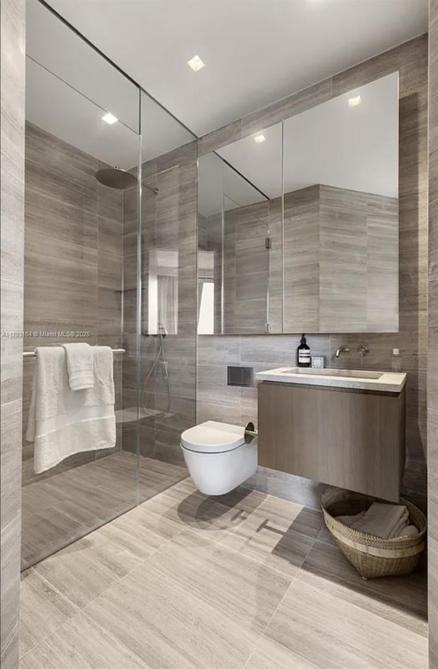bathroom featuring vanity, toilet, tile patterned floors, tile walls, and tiled shower