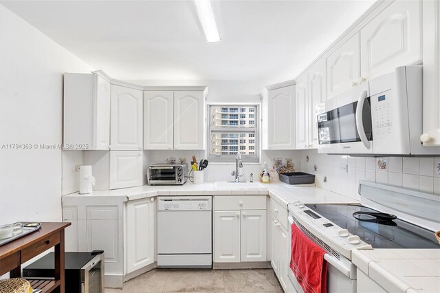 kitchen with tile countertops, tasteful backsplash, a sink, white cabinets, and white appliances