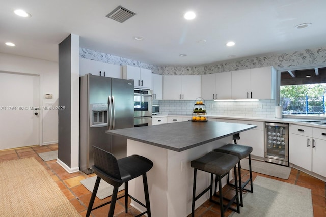 kitchen featuring appliances with stainless steel finishes, a breakfast bar area, tasteful backsplash, wine cooler, and visible vents