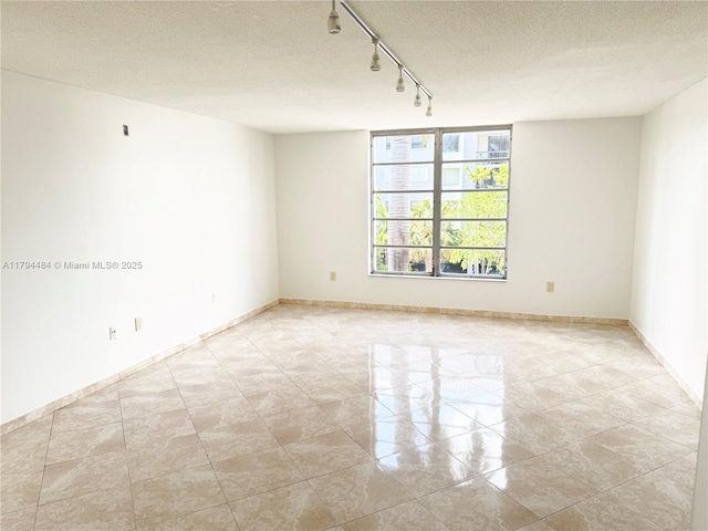 unfurnished room with baseboards, rail lighting, and a textured ceiling