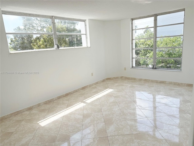 empty room with baseboards, plenty of natural light, and tile patterned flooring