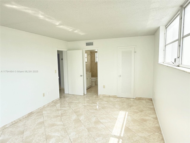 unfurnished bedroom featuring a textured ceiling, visible vents, baseboards, ensuite bath, and light tile patterned flooring