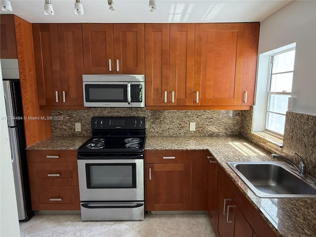 kitchen with dark stone counters, stainless steel appliances, decorative backsplash, and a sink