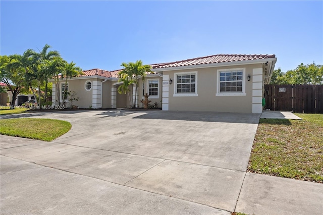 mediterranean / spanish home with concrete driveway, fence, a tile roof, and stucco siding