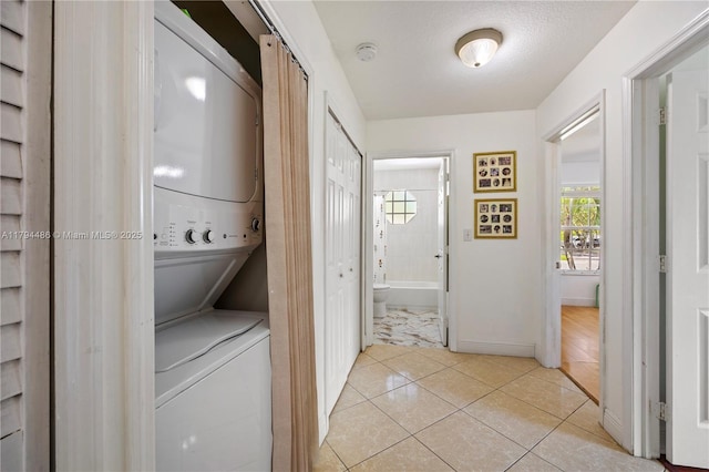 laundry area with baseboards, stacked washer and clothes dryer, light tile patterned flooring, and laundry area