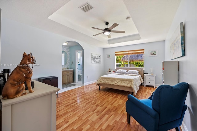 bedroom with visible vents, arched walkways, baseboards, light wood finished floors, and a tray ceiling