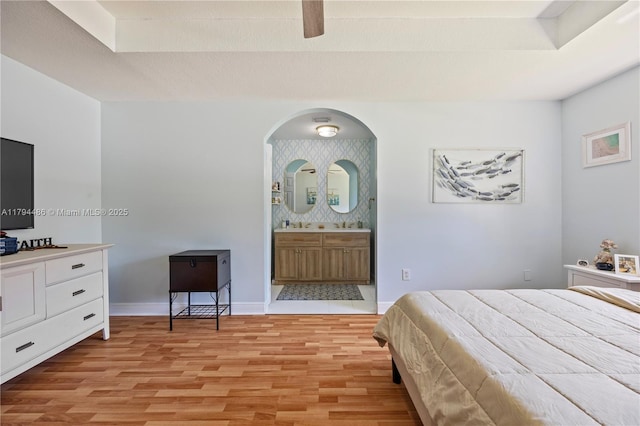 bedroom featuring connected bathroom, arched walkways, light wood-style flooring, and baseboards
