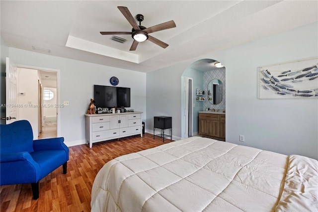 bedroom with arched walkways, baseboards, wood finished floors, a tray ceiling, and visible vents