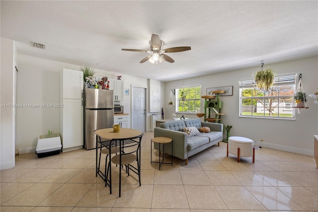 living room featuring ceiling fan, a textured ceiling, visible vents, light tile patterned floors, and baseboards