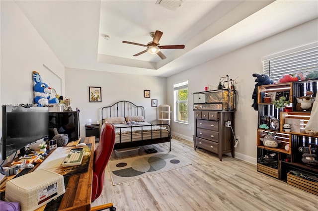 bedroom with visible vents, wood finished floors, baseboards, a tray ceiling, and a ceiling fan