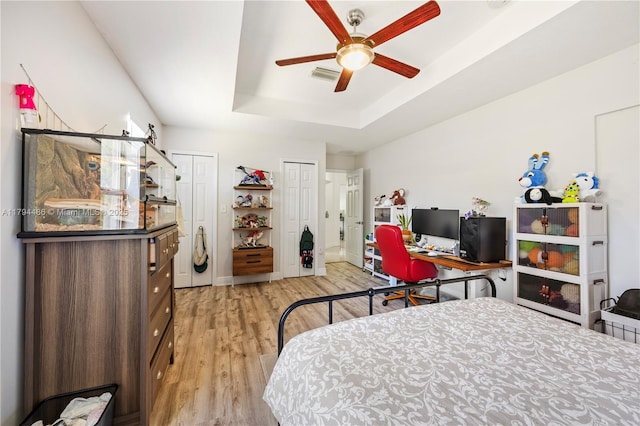 bedroom with multiple closets, a tray ceiling, light wood finished floors, and visible vents