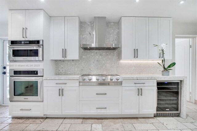 1161 Sunset Dr, Coral Gables, FL 33143 - kitchen with wine cooler, wall chimney exhaust hood, light countertops, stainless steel appliances, and white cabinets