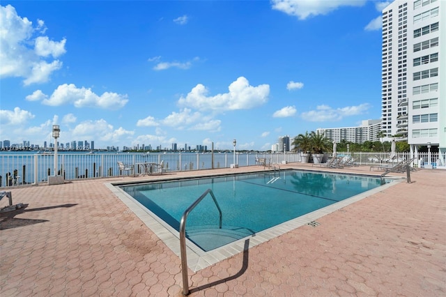 community pool with a patio, fence, and a city view