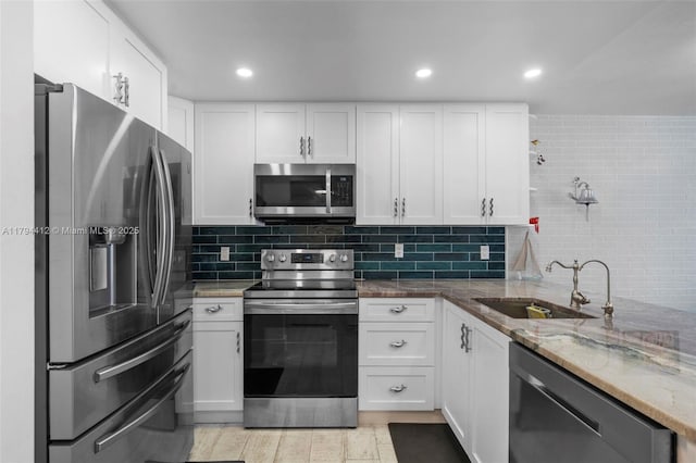 kitchen with decorative backsplash, white cabinets, light stone counters, a sink, and stainless steel appliances