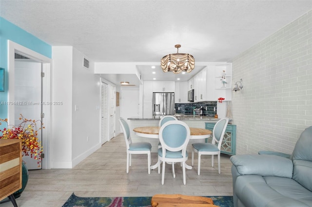 dining room with visible vents, brick wall, baseboards, a chandelier, and light wood finished floors