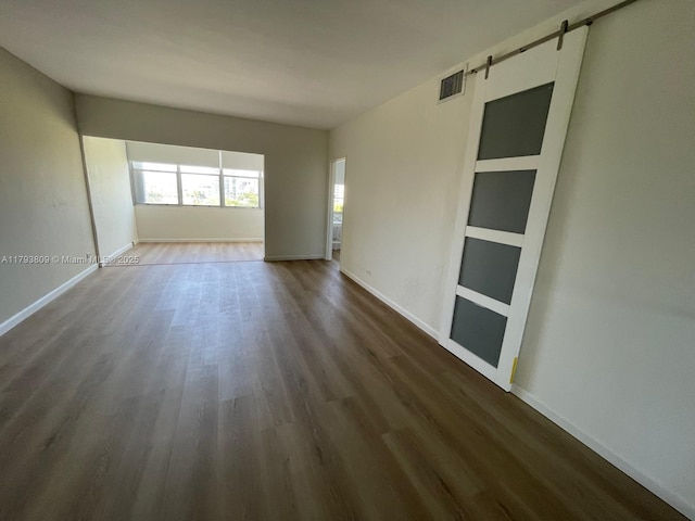 empty room featuring visible vents, dark wood-style flooring, and baseboards