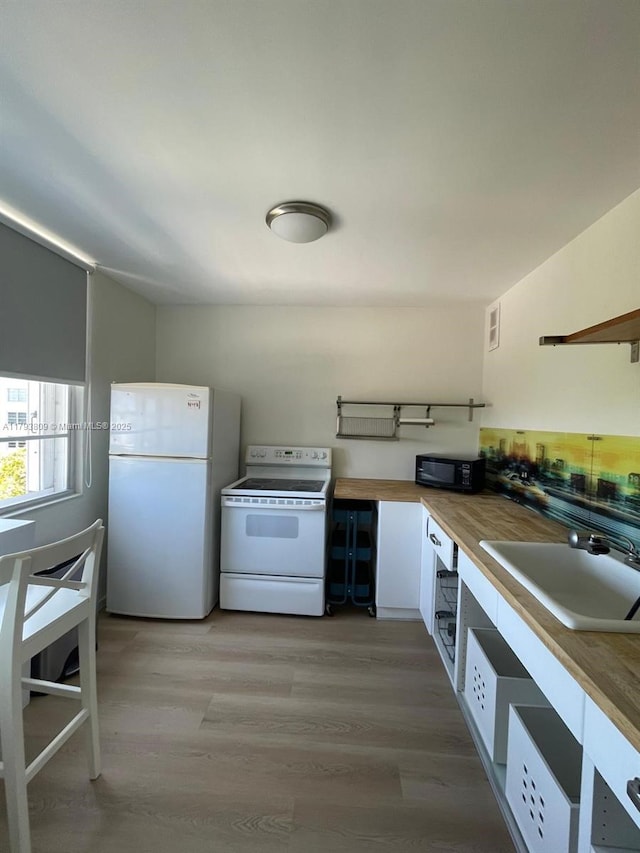 kitchen with white appliances, butcher block countertops, light wood-style floors, white cabinetry, and a sink