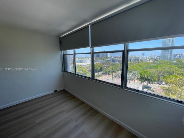 unfurnished room with baseboards, a city view, and wood finished floors