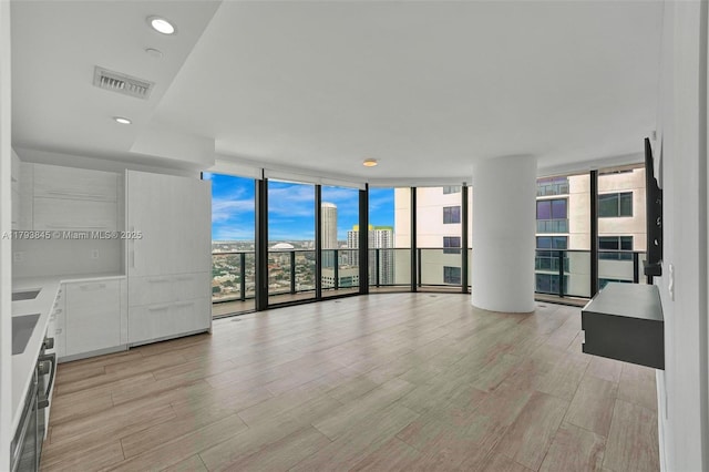 unfurnished living room with visible vents, a wall of windows, and light wood-style floors
