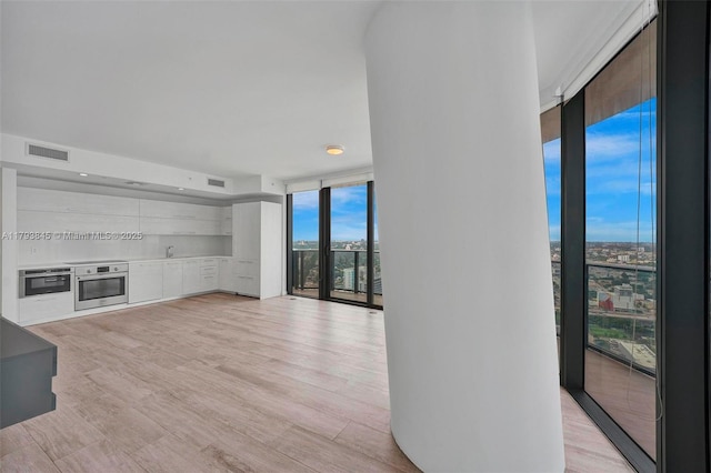 unfurnished living room with a wall of windows, light wood finished floors, and visible vents