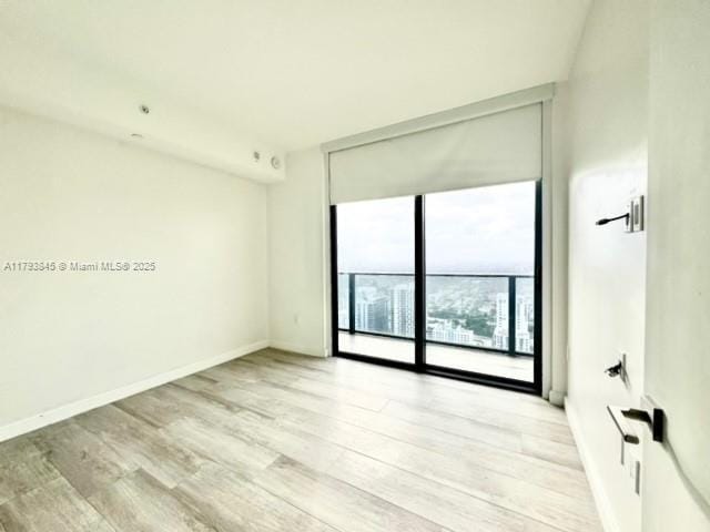 spare room featuring baseboards, a wall of windows, and wood finished floors