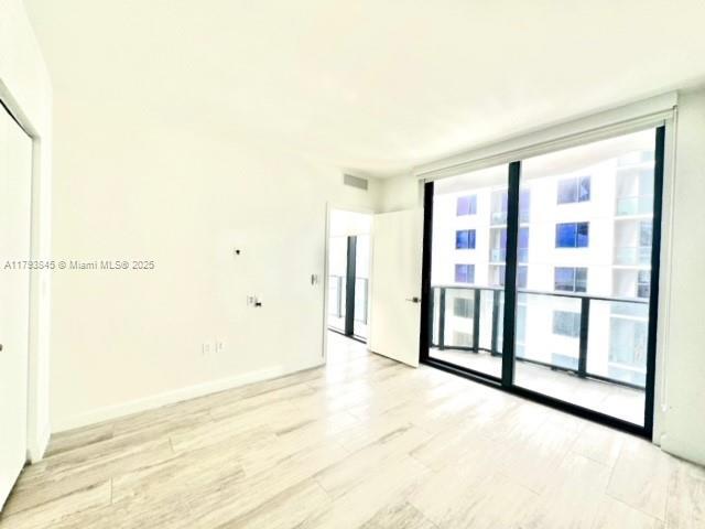 unfurnished room featuring baseboards, floor to ceiling windows, light wood-style flooring, and visible vents