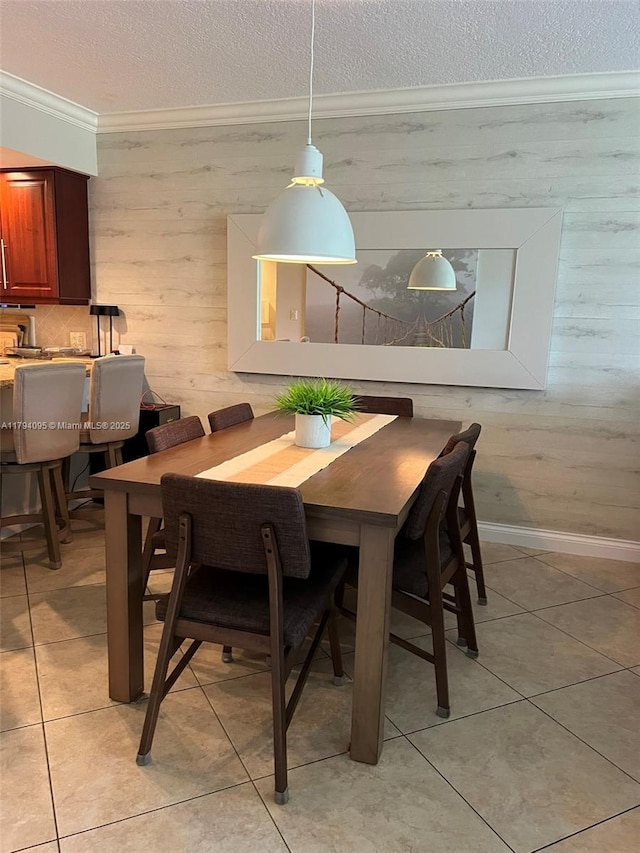 dining room with a textured ceiling, wood walls, baseboards, ornamental molding, and light tile patterned flooring