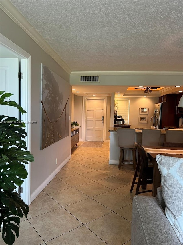 hallway featuring crown molding, light tile patterned floors, a textured ceiling, and visible vents