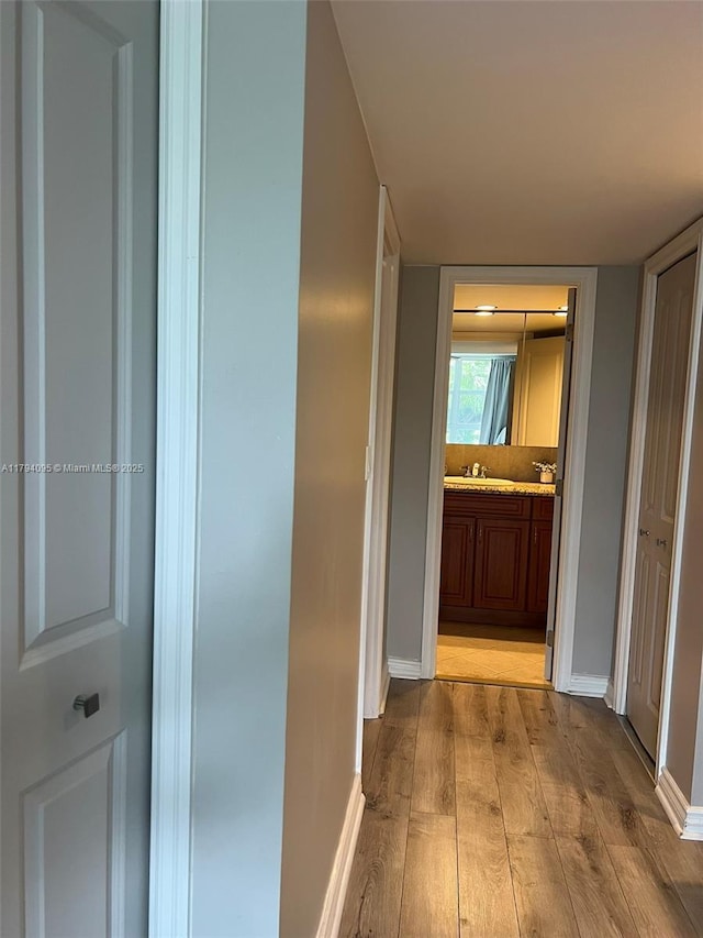 corridor with baseboards, a sink, and wood finished floors