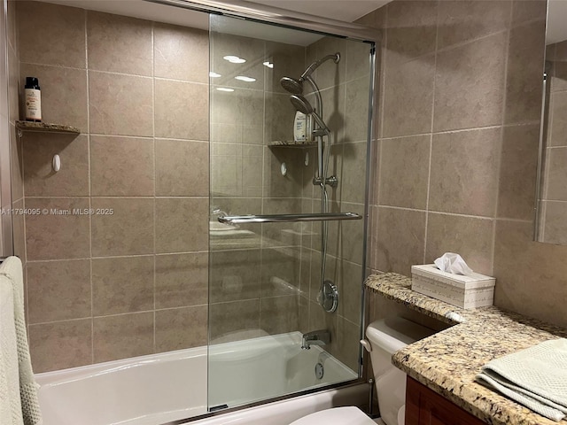 bathroom featuring vanity, tile walls, combined bath / shower with glass door, and toilet