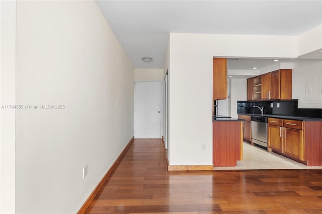 kitchen featuring stainless steel dishwasher, brown cabinetry, light wood-style floors, and dark countertops