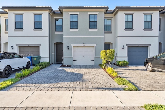 townhome / multi-family property with stucco siding, decorative driveway, a tile roof, and a garage