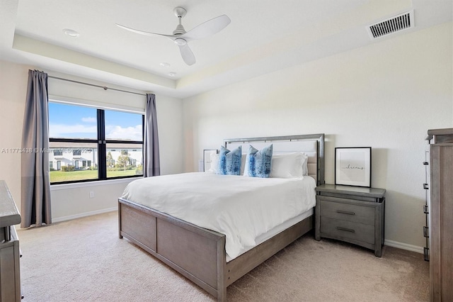 bedroom with a ceiling fan, visible vents, baseboards, a raised ceiling, and light carpet