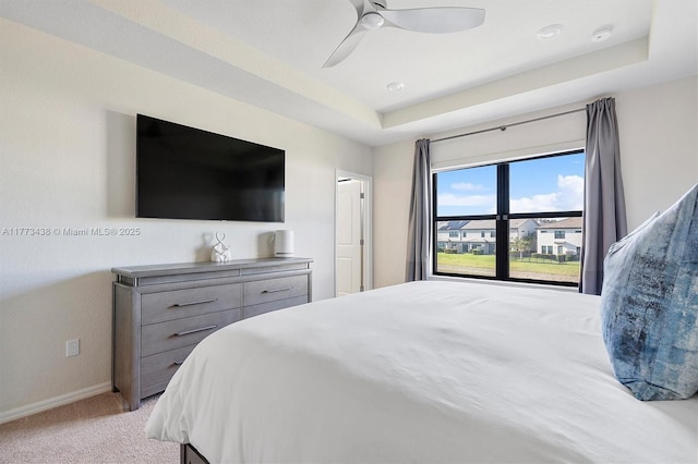 bedroom with baseboards, ceiling fan, light carpet, and a tray ceiling