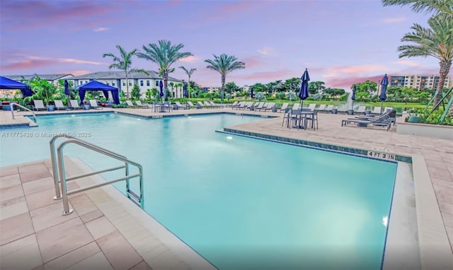 pool at dusk with a community pool and a patio