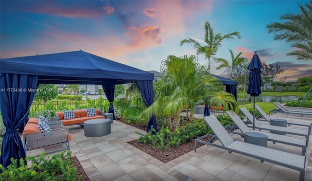 patio terrace at dusk with a water view, fence, a gazebo, and an outdoor living space