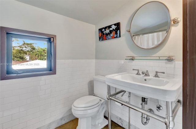 bathroom featuring a wainscoted wall, toilet, and tile walls