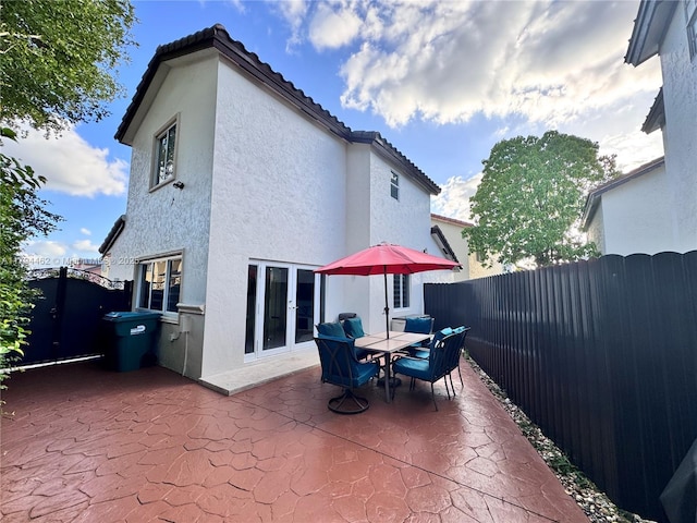 rear view of property featuring fence, a patio, stucco siding, french doors, and a tiled roof