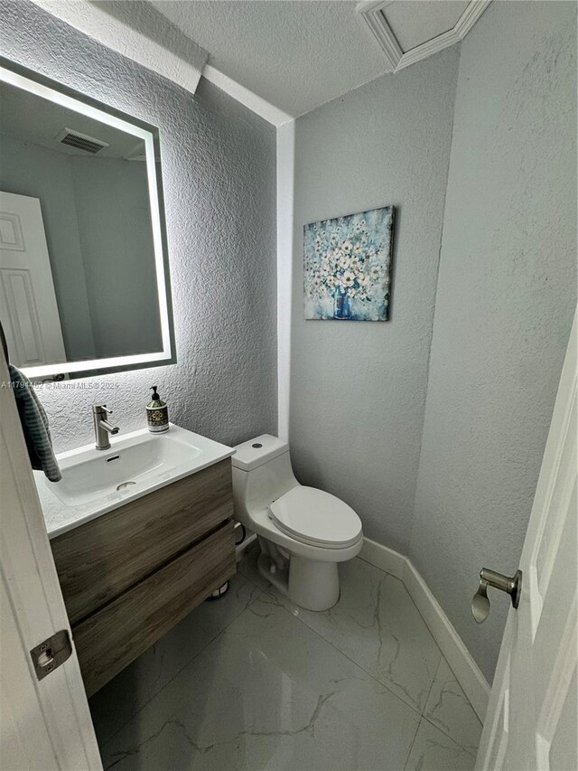 half bath featuring toilet, a textured wall, baseboards, and marble finish floor