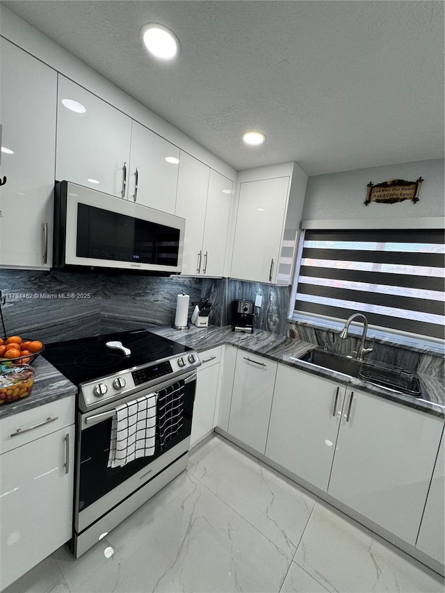 kitchen with decorative backsplash, marble finish floor, dark countertops, white microwave, and stainless steel range with electric cooktop