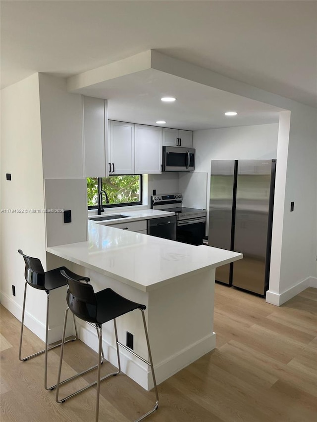 kitchen featuring a peninsula, baseboards, light wood-type flooring, a sink, and appliances with stainless steel finishes