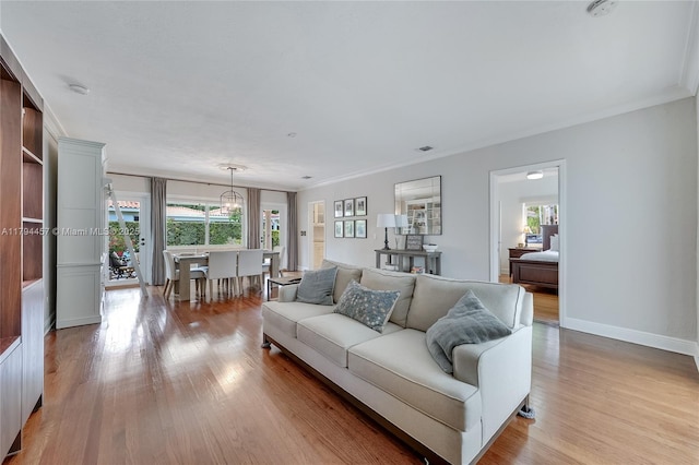 living room featuring an inviting chandelier, baseboards, ornamental molding, and light wood-type flooring