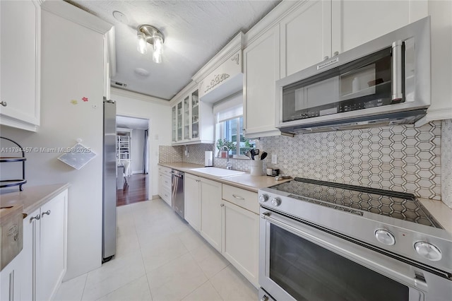 kitchen with stainless steel appliances, white cabinetry, a sink, and glass insert cabinets