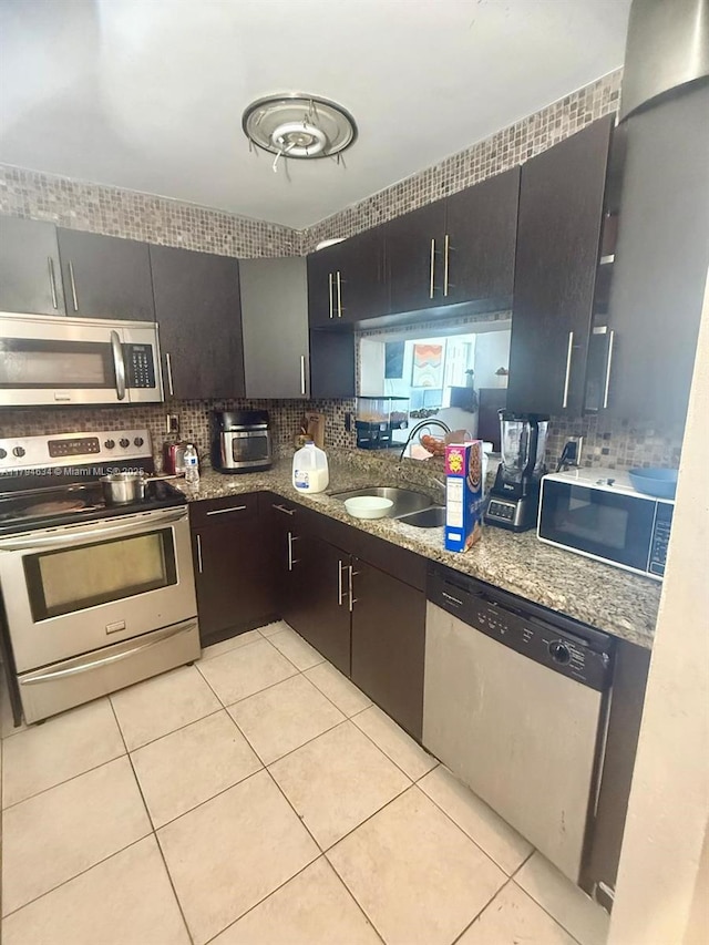 kitchen featuring light tile patterned flooring, a sink, stone countertops, stainless steel appliances, and backsplash