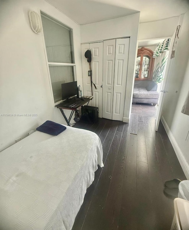 bedroom featuring dark wood-style flooring, baseboards, and a closet