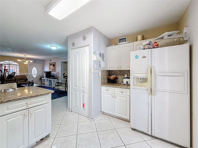 kitchen with decorative backsplash, light tile patterned flooring, white refrigerator with ice dispenser, white cabinets, and a chandelier