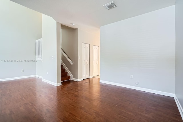 unfurnished room featuring stairs, dark wood-style flooring, baseboards, and visible vents